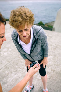 High angle view of mother and daughter looking at smart watch while standing on pier