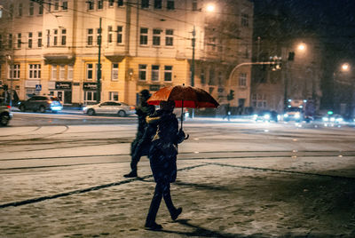Rear view of woman carrying umbrella during snowfall in city at night