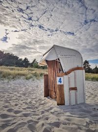 Hooded beach chairs on sand against sky