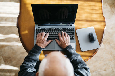 Senior man using laptop at home, top view