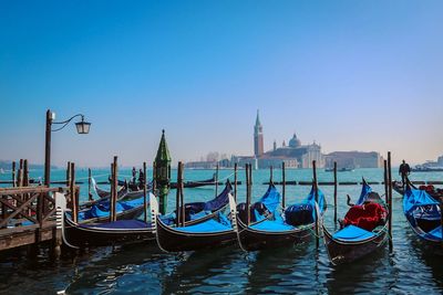 Boats moored in canal against clear blue sky