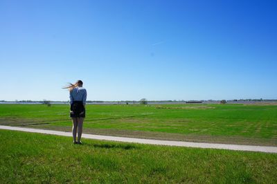 Rear view of woman standing on grassy field against sky during sunny day
