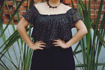 Midsection of woman with hands on hip standing against plants