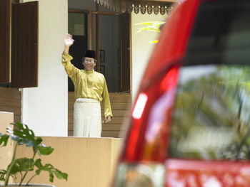 Portrait of man waving while standing outside house