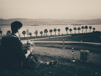 Man sitting on shore against sky