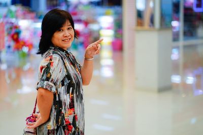 Portrait of woman pointing while standing in mall