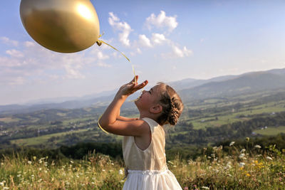 Woman holding balloons on field against sky