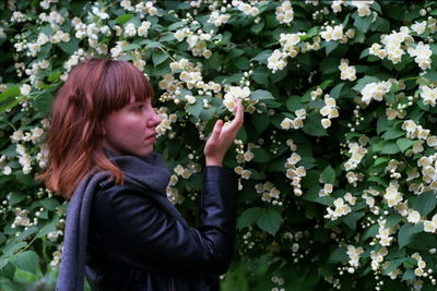 Side view of young woman touching white flowers blooming outdoors