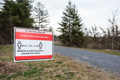 Covid 19 sign on edge of wooded walking trail warning to stay apart.