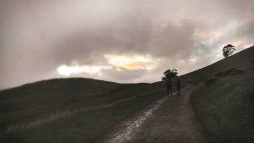 People on country road against cloudy sky