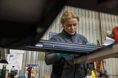 Side view of young woman using mobile phone while standing in factory