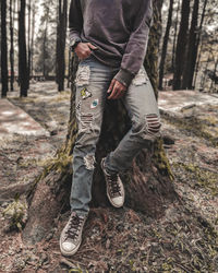 Low section of man standing by tree trunk in forest