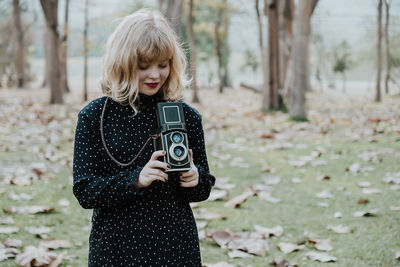 Young woman photographing from camera while standing on field