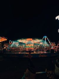 Rear view of people at amusement park against sky at night
