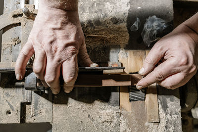 Crop male woodworker standing at old workbench and working with lumber details in grungy workshop