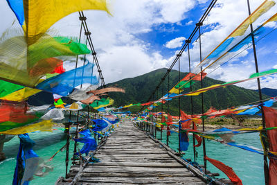 Prayer flags hanging on railing of bridge against mountain