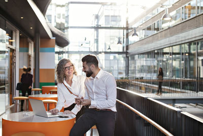 Smiling business colleagues discussing over laptop at atrium