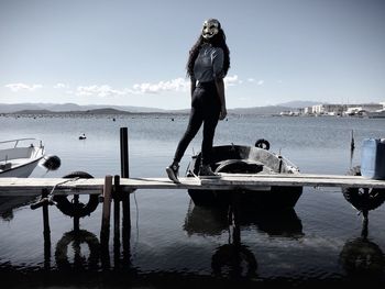 Rear view of woman wearing mask standing on jetty over sea against sky
