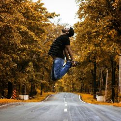 Man jumping on road amidst trees during autumn