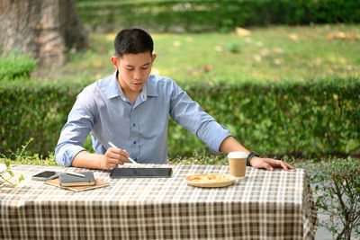 Side view of man using digital tablet while sitting at park