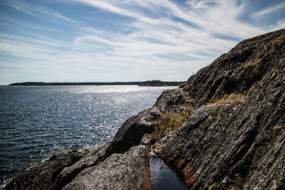 Rock formation by sea against sky on sunny day