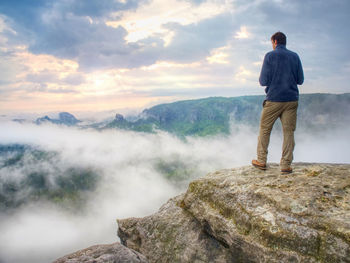 Photographer on mountain cliff looking into mist. hiker will take picture with small camera in hands