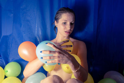 Shirtless woman with colorful balloons at home