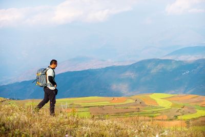 Hiker walking on field against mountain range