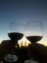 Close-up of hand holding glass against sky