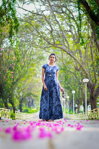 Portrait of young woman standing on road amidst trees