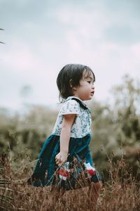 Girl looking away on field against sky