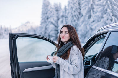 Portrait of young woman standing against car