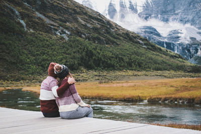 Rear view of couple sitting on lake against mountains