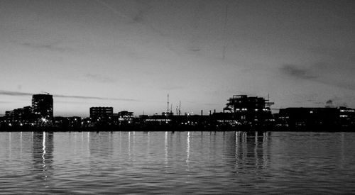 Illuminated buildings by sea against sky at night