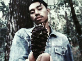Portrait of man holding ice cream on tree trunk in forest