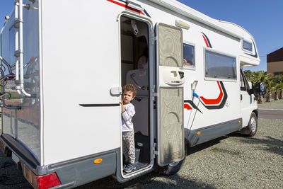 Curly haired boy at the door of his motorhome on a sunny morning dressed in his pajamas