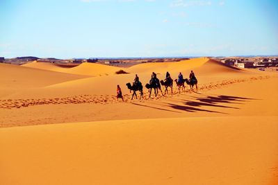 People walking on sand dune in desert against sky