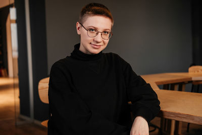 Young woman with short hair in eyeglasses and black sweater sitting at the table in office