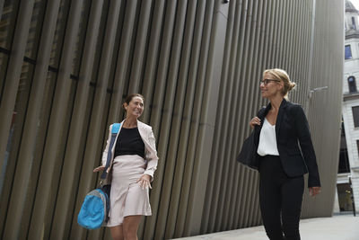 Smiling female colleagues talking while walking by office building in downtown