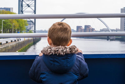 Rear view of boy standing on bridge over river