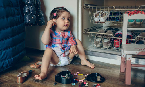 Full length of cute girl playing with toys while sitting on hardwood floor at home