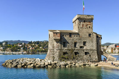 Buildings by sea against clear blue sky