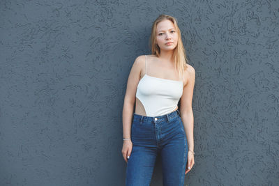 Portrait of a young woman standing against wall