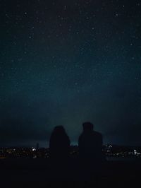 Rear view of couple gazing at a starry sky and city lights at night