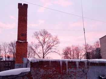 Bare tree and buildings against sky during winter