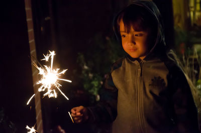Close-up of cute boy holding sparkler at night