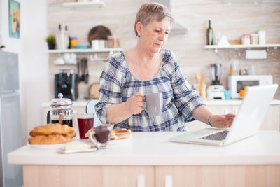 Senior woman having coffee while using laptop at home