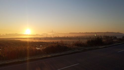 Road amidst field against sky during sunset