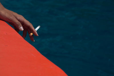 Cropped hand of woman holding cigarette against sea