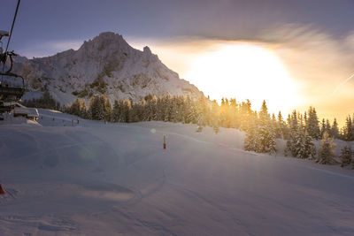 The sun rising behind the trees over a snowy slope in les arcs